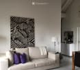 Modern living room with a beige sofa, purple cushions, a white coffee table with a glass bowl, a floor lamp, and a large zebra print wall art.