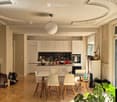 Open-plan kitchen and dining area with modern white cabinets, a central island, a dining table with four chairs, and various kitchen appliances and decor items.