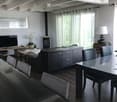 Modern living room with a grey sofa, coffee table, fireplace, dining area with a glass table and chairs, and a TV on a wooden stand.