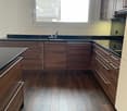 Modern kitchen with wooden cabinets, dark countertops, and a large window overlooking a roof.