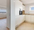 Modern kitchen with white cabinets, light wood flooring, and large windows offering a scenic view.