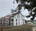 Modern two-story house with white exterior, large windows, and balconies. The house features a flat roof and contemporary design.