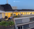 Rooftop terrace with modern furniture, umbrella, plants, and city view.