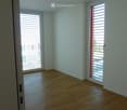 Empty room with light-colored wooden flooring and white walls, featuring two large windows with blinds and a door leading to an outdoor area.