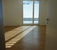 Empty room with wooden flooring and large sliding glass doors with blinds, allowing natural light to create striped shadows on the floor.