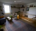 Bright living room with wooden flooring, large window, colorful rug, sofa, coffee table, armchair, ottoman, and decorative plants.