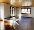 Empty room with wooden and tiled flooring, large windows, and a sliding glass door leading outside.