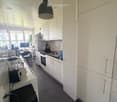 Modern kitchen with white cabinets, dark tiled floor, microwave, oven, refrigerator, sink, blender, and a small table with chairs in the adjacent room.