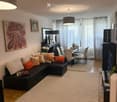 Modern living room with a black sectional sofa, colorful cushions, a dining area with chairs and a table, a large mirror, and artwork on the walls.