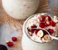 Two glass jars filled with a creamy oatmeal mixture topped with pomegranate seeds and sliced almonds, placed on a woven mat with scattered pomegranate seeds and almonds around.