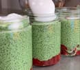 Four mason jars filled with layered green smoothie mixtures topped with whipped cream, placed on a countertop.