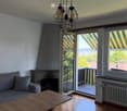 Modern living room with wooden flooring, grey sofa, coffee table, fireplace, large windows, and a view of the landscape.