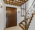 Elegant hallway with a wooden door, ornate wall-mounted candle holders, and a staircase with a decorative wrought-iron railing and wooden steps.