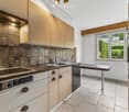 Modern kitchen with light wooden cabinets, stainless steel appliances, and a central island table.