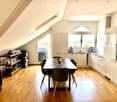 Bright, modern kitchen and dining area with wooden flooring, white cabinets, and large windows offering a scenic view. Includes a dining table with chairs, a microwave, and various kitchen appliances.