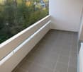 Balcony with tiled floor, white railing, and view of greenery and trees.