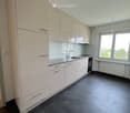 Modern kitchen with white cabinets, granite countertop, dark tiled floor, and large windows.