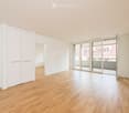 Empty room with light wooden flooring, white walls, large sliding glass doors leading to a balcony, and built-in white closet units.