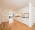 Modern kitchen with white cabinets, wooden flooring, and a sleek sink area. Features include built-in lighting and a sliding glass door leading to a balcony.
