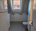 Bathroom with a toilet, shower, sink, white tiles and wood floor
