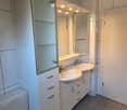 Bathroom with tiled walls, white sink, mirror, modern bathroom cabinet, toilet.