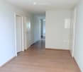 Empty hallway with light wooden flooring, white walls, and several closed doors leading to other rooms.