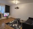 Modern living room with wooden flooring, large window with curtains, grey sofa, coffee table, TV, and decorative wall art.
