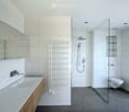 Modern bathroom with a large sink, toilet, shower, radiator, and mirror. The space features white tiles and a sleek design.