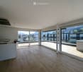 Bright, open-plan room with wooden flooring, large glass sliding doors leading to a balcony, and a scenic mountain view.