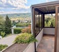 Balcony with tiled floor, large windows, and scenic view of a town and river valley.