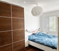 Modern bedroom with a white bed, blue bedding, a wooden wardrobe, and a round pendant light.