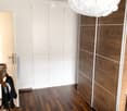 Modern hallway with wooden flooring, white walls, built-in wooden closet, and a large spherical light fixture hanging from the ceiling.