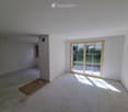 Empty room with white walls, concrete floor, large sliding glass door leading to outdoor area, small window, and a wooden plank on the floor.