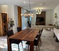 Modern open-plan living and dining area with a wooden dining table, black chairs, a light-colored sofa, a TV, a wooden cabinet, and decorative vases.