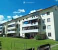 Modern multi-story residential building with balconies, large windows, and a well-maintained lawn in front.