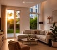 Modern living room with a large sectional sofa, coffee table, armchair, floor lamp, and large windows with sheer curtains. The space features a light-colored carpet, wooden flooring, and decorative plants.