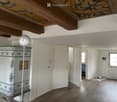 An unfurnished room with wooden flooring, white walls, and a decorative cabinet. The room features a large window, a door leading to another space, and a modern spherical lamp on a stand.