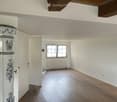 Empty room with wooden flooring, white walls, and a window with white frame. Exposed wooden beams on the ceiling.