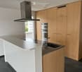 Modern kitchen with light wooden cabinets, a white kitchen island, granite countertop, stainless steel sink, and built-in oven.
