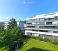 Modern multi-story residential building with balconies, large windows, and surrounding greenery including a playground area.