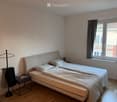 A tidy bedroom with a double bed, nightstand, clothing rack, and window with curtains.