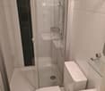 Modern bathroom with white tiles, a bathtub, toilet, sink, and a glass-enclosed shower area.