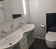 Modern bathroom with white tiles, black accents, double sink vanity, chrome faucets, and a toilet.