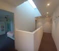 Bright hallway with a skylight ceiling, white walls, and carpeted floors. Features a raised section leading to a bedroom area with a bed and wardrobe visible in the background.