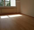 Empty room with wooden flooring, large window with blinds, radiator, and natural light streaming in.