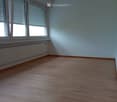 Empty room with wooden flooring, white walls, large windows with blinds, and a radiator under the windows.