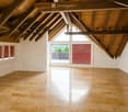 Bright, open room with wooden ceiling beams, large windows, and light-colored tile flooring. No furniture or furnishings are present.