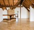 Open-concept living room with exposed wooden beams, a stone fireplace, and polished tile flooring.