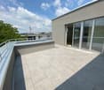 Modern rooftop terrace with tiled flooring, metal railing, and large glass sliding doors leading to an indoor space.