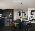 Modern dining area with a round glass table, four chairs, a pendant light, and a vase with flowers. The space is connected to a kitchen area with dark cabinets and a coffee machine.